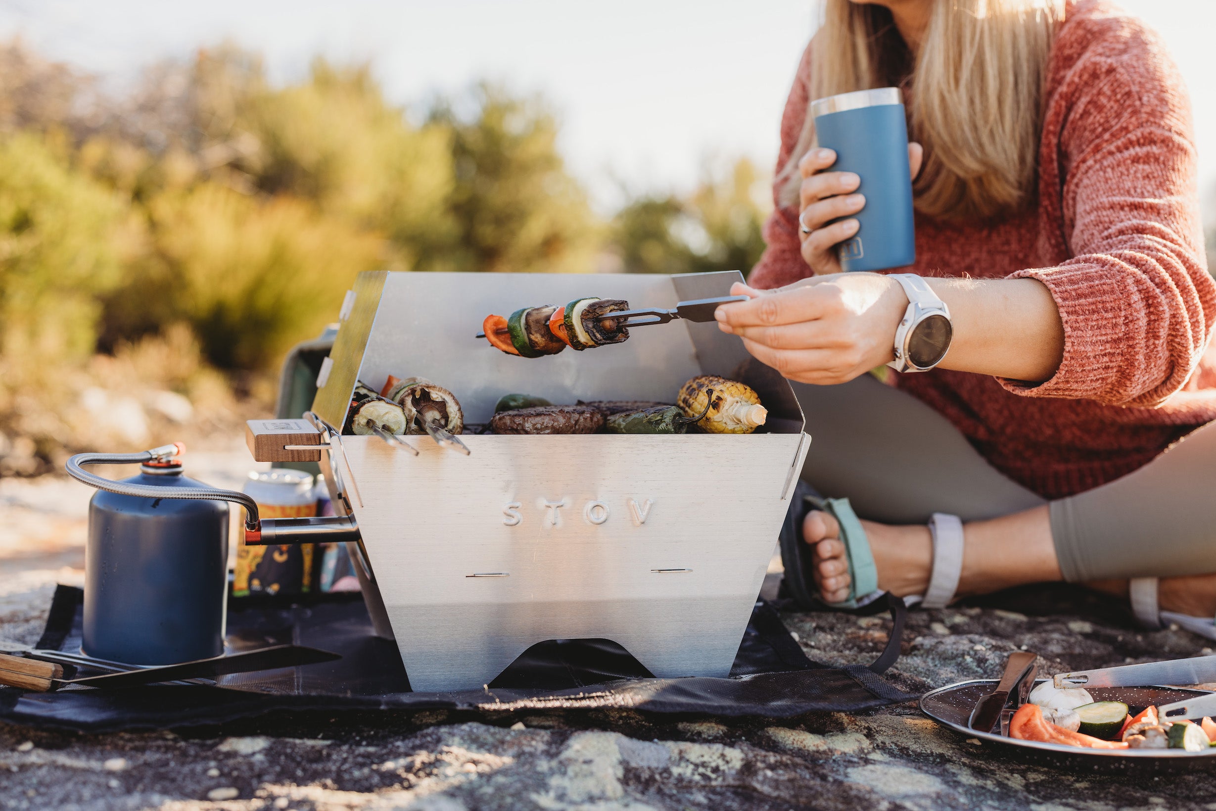 BBQing on the portable STOV gas BBQ holding a skewer with delicious food ready to be eaten.